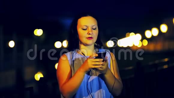 一位戴着耳机的年轻女子在堤岸和夜空的背景上听音乐唱歌视频的预览图