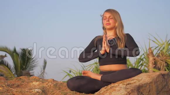 穿着运动服的女士坐在灰色岩石悬崖上做瑜伽姿势视频的预览图