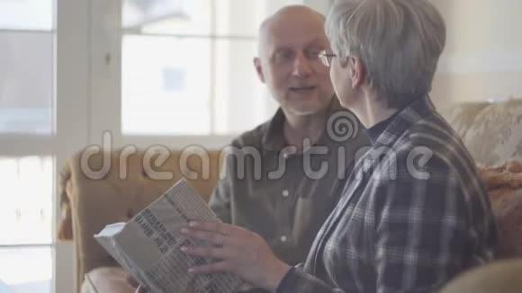 老夫妇男人和女人坐在沙发上拿着一本书互相交谈和微笑家庭关系视频的预览图