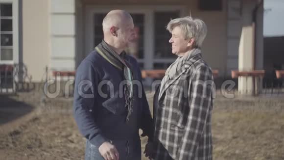 快乐的老夫妇秃顶的男人和女人穿着外套戴着围巾站在房子附近男人展示着钥匙视频的预览图