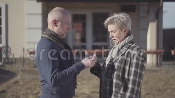 幸福的老夫妇秃顶的男人和女人灰色的短发外套和围巾站在房子附近一位女士在视频的预览图