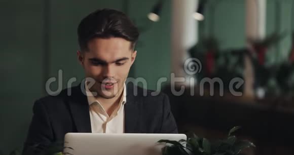 快乐的年轻商人坐在咖啡馆里用笔记本电脑工作胜利者看着手提电脑显示出是的姿态庆祝视频的预览图