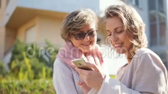 成年的女儿和她的中年母亲站在街中央的智能手机里看照片视频的预览图