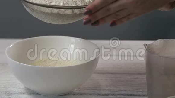 特写镜头慢动作女人手把面粉从一个筛子中筛入白色碗视频的预览图