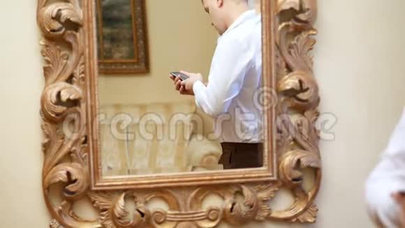 镜子里的倒影英俊的男人穿着白色衬衫的商人拿着智能手机年轻人视频的预览图