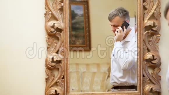 镜子里的倒影年轻的商人穿着白色衬衫手里拿着智能手机视频的预览图