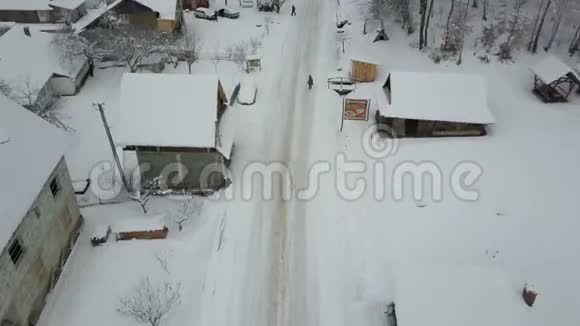 快速飞越喀尔巴阡村的一条公路鸟雪覆盖的房子的视野冬季的乡村景观视频的预览图