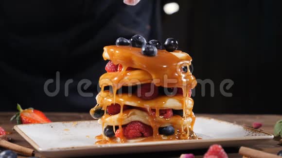 烹饪艺术在家或家中享用美味的有机薄煎饼时厨师用手浇上森林浆果的特写镜头视频的预览图
