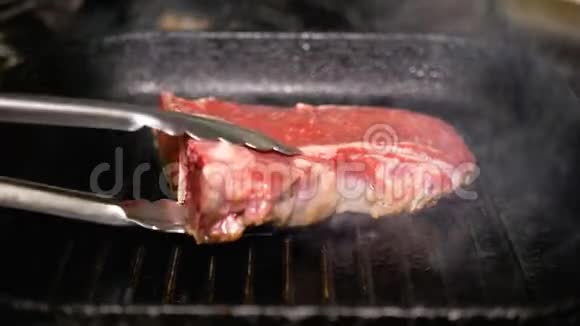 一块生肉用金属钳在烤盘上转动烹饪T面牛排特写美味的脂肪垃圾食品视频的预览图