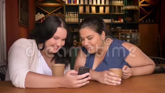 肥胖的白种人两个女朋友瞥了一眼智能手机喝了几杯咖啡情绪激动视频的预览图