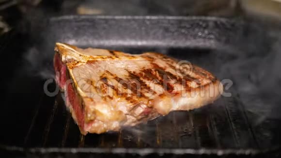 一块肉用铁钳把骨头翻过来放在烤盘上烹饪T面牛排特写美味的脂肪视频的预览图