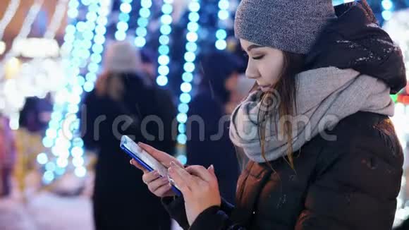 美丽的女人在下雪的夜晚圣诞节和新年使用手机应用程序视频的预览图