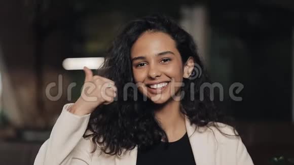 美丽的年轻女子展示拇指向上和微笑站在舒适的咖啡馆工作中的少女竖起大拇指视频的预览图