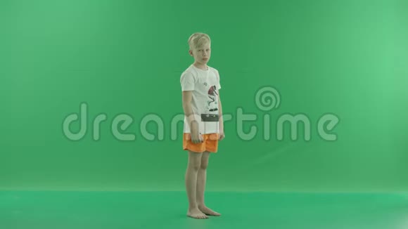 一个身穿便服的金发小男孩正竖起大拇指他侧着身子站在绿色屏幕上视频的预览图