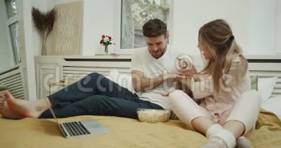 舒适风格的卧室年轻夫妇在床上一起吃爆米花和互相玩玩得很开心4k视频的预览图