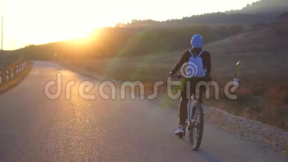 穆斯林妇女戴头巾背着背包骑自行车在路上夕阳西下后景视频的预览图