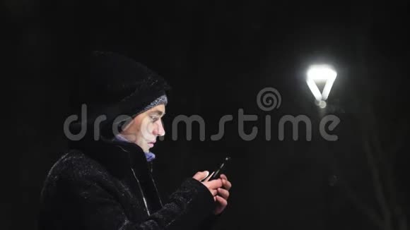 街灯里的那个人那家伙看着他的智能手机在灯的背景下下雪慢动作视频的预览图