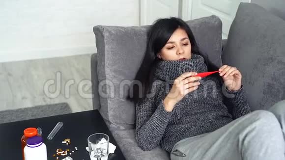 年轻女子测量坐在家里沙发上的温度女人在病毒或感冒时感到不快乐视频的预览图