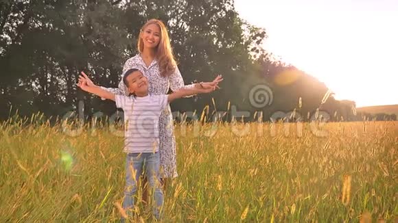 快乐的亚洲妈妈背着她可爱的小男孩手牵手在夕阳下的黄色田野上微笑视频的预览图