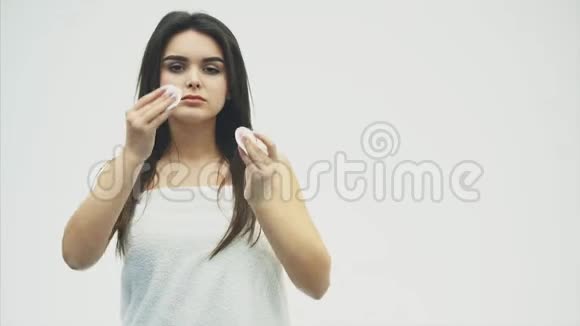 一个迷人的年轻白种人微笑的黑发女孩的特写肖像被孤立在白色背景上把她的脸擦干净视频的预览图