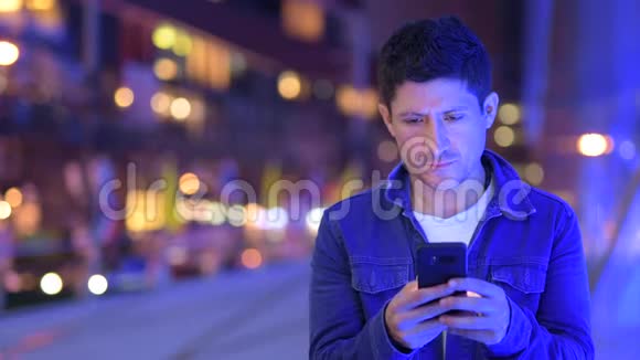 快乐的西班牙男人晚上在城市街道上用电话视频的预览图
