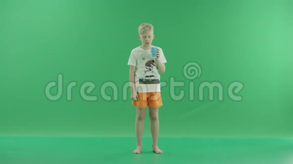 一个年轻的金发男孩喝水是为了在炎热的日子里提神他站在绿色屏幕前视频的预览图