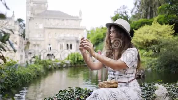 戴帽子的微笑女人在水边的智能手机上自拍视频的预览图