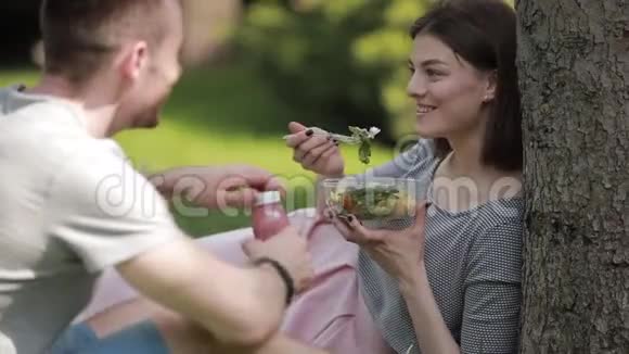 年轻的素食夫妇坐在公园里吃沙拉和喝冰沙视频的预览图