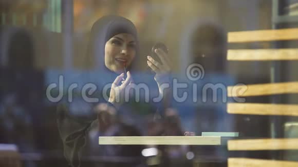 漂亮自信的穆斯林女士在咖啡馆里涂口红微笑着视频的预览图