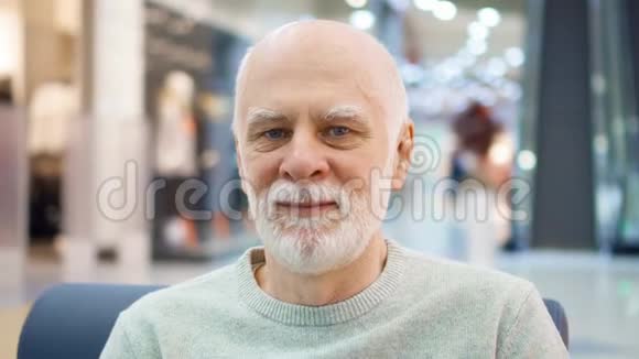 坐在商场里看摄像机的老人的肖像购物中心的男购物者微笑着视频的预览图