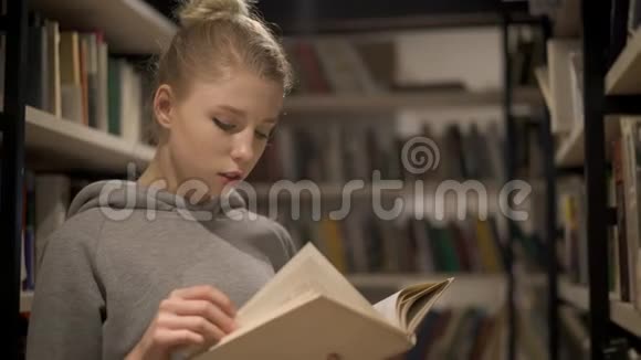 一个年轻的金发女孩在图书馆的书架间看书视频的预览图