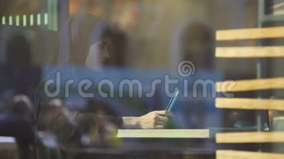 戴着头巾的漂亮女士在平板电脑上工作坐在咖啡馆里自由职业项目视频的预览图