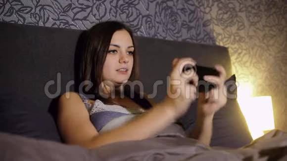 年轻女性在晚上躺在家里的床上玩智能手机游戏紧张的比赛赢得比赛视频的预览图