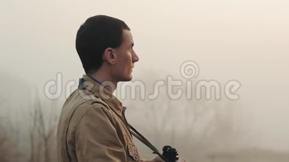 一个身穿卡其色外套的年轻红发男子手持望远镜看日出和日落四周都是雾视频的预览图