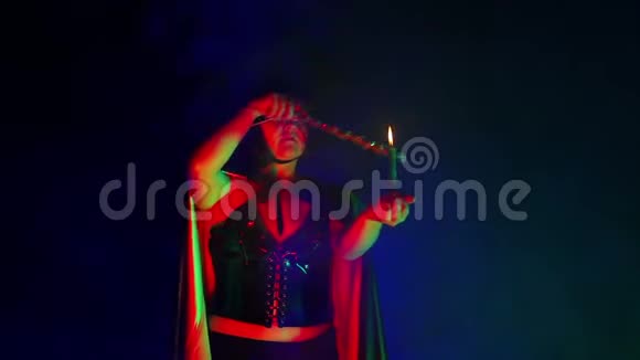 一个身穿黑斗篷手里拿着蜡烛的烟云的年轻女巫正在用魔杖施展魔法视频的预览图