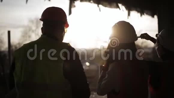 在夕阳的照耀下领班在工地上与女检查员交谈建筑工人剪影视频的预览图