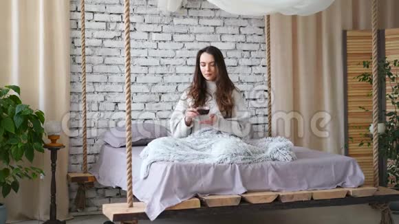 年轻漂亮的女人在家里的床上喝着香气扑鼻的咖啡视频的预览图