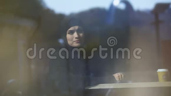 美丽体贴的穆斯林女士坐在咖啡馆里戴着头巾等待点菜视频的预览图