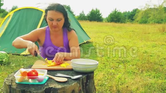一个女人在矮矮的桌子旁的帐篷里用一把小刀在木板上把黄胡椒切成小块视频的预览图
