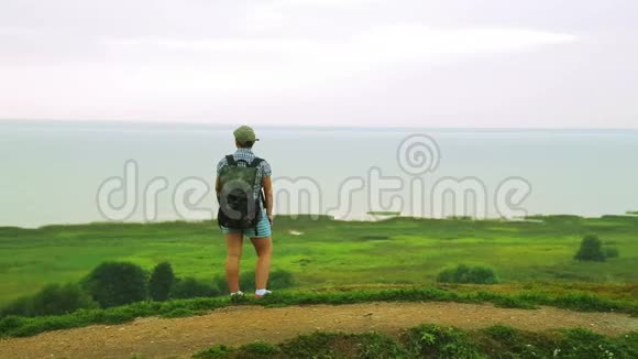 背着背包的女旅行者站在山的边缘在雨中欣赏湖总体情况视频的预览图
