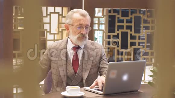 一个老商人他的办公室概念是在咖啡休息时带着笔记本电脑视频的预览图