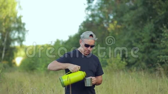 一个在森林里的男性游客从热水瓶里倒入一杯茶视频的预览图