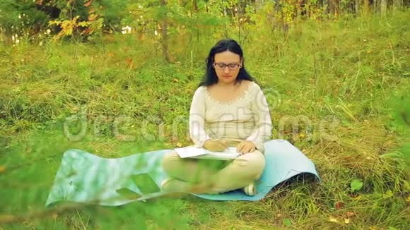 一个在森林边缘戴眼镜的黑发女人用铅笔画图表视频的预览图