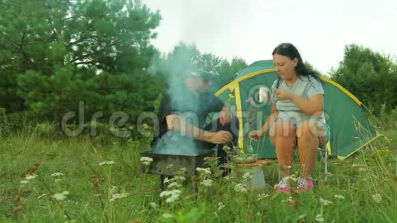 男人和女人的游客坐在吸烟烧烤旁边吃和喝茶视频的预览图
