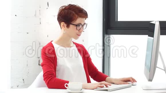 年轻妇女在办公室工作坐在办公桌前用电脑看屏幕视频的预览图