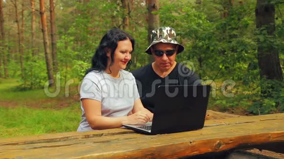 公园里的男人和女人坐在长凳上男人在笔记本电脑屏幕上显示女人视频的预览图