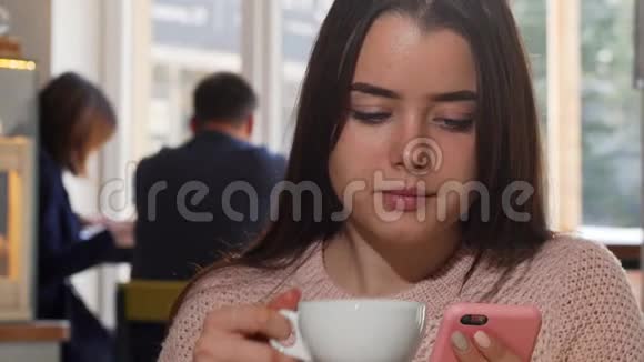 迷人的女人喝咖啡在咖啡馆用她的智能手机视频的预览图