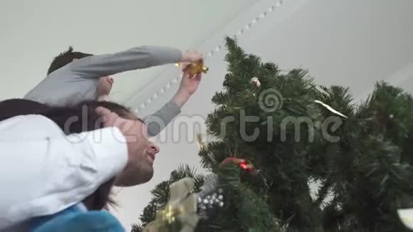快乐的孩子把圣诞玩具挂在树上坐在他父亲的脖子上父子关系视频的预览图