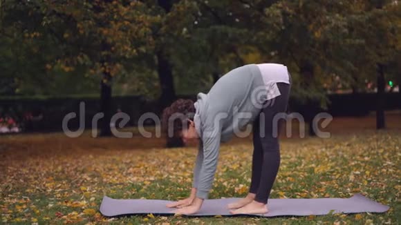 美丽的黑发正在练习巴卡萨纳平衡双手瑜伽垫独自在公园锻炼现代青年视频的预览图