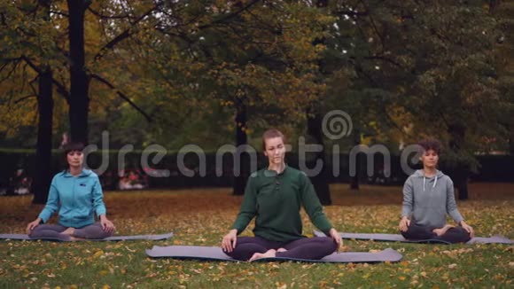女性瑜伽教练展示伸展运动然后在莲花位置放松闭着眼睛坐在垫子上视频的预览图